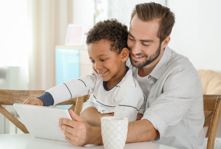 Image is of a father with his son on his lap while both are looking at a tablet, concept of establishing parental rights in Tennessee