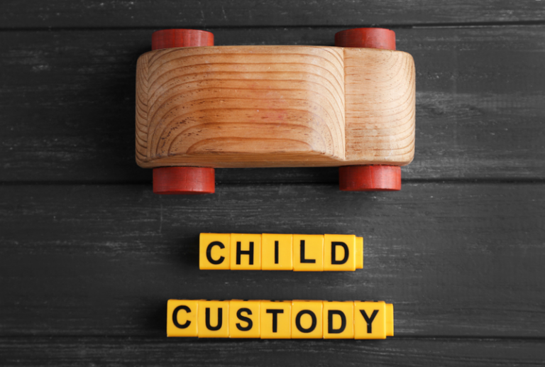 Image is a top-down view of a wooden toy car and yellow alphabet blocks spelling 'child custody', concept of how to get full custody in Tennessee