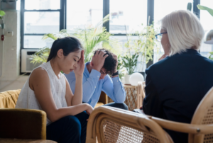 Image is of a young married couple looking upset and troubled, possibly fighting, while speaking to a therapist, concept of "Does it Matter Who Files for Divorce First in Franklin TN?"