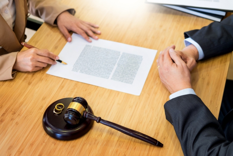 Image is of a woman signing a divorce paper while sitting across from a divorce lawyer, concept of do I need a divorce lawyer?