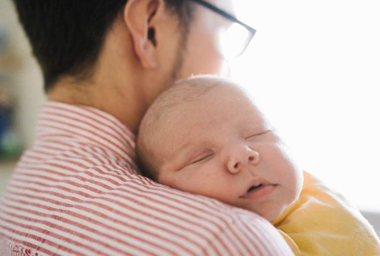 Image is a closeup of a sleeping baby's face laying on the shoulder of a man, concept of establishing paternity in Tennessee