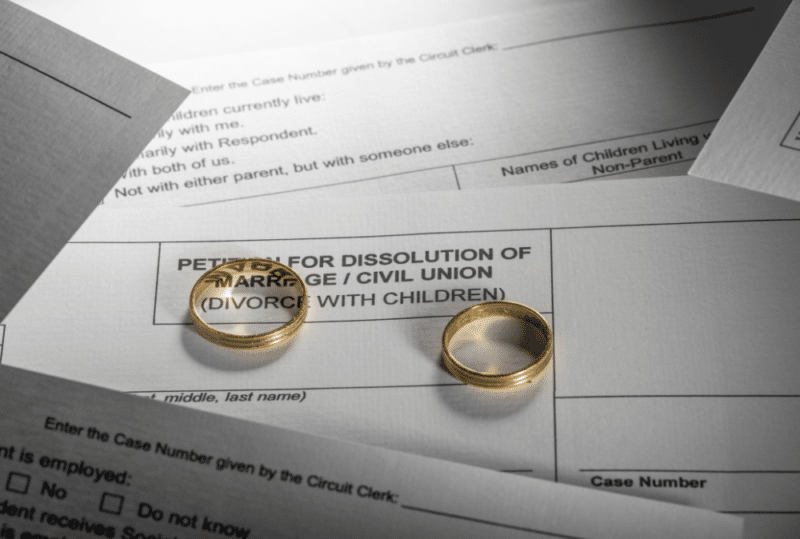 Image is of a pair of wedding bands laying on top of divorce forms, concept of guide to Tennessee divorce forms
