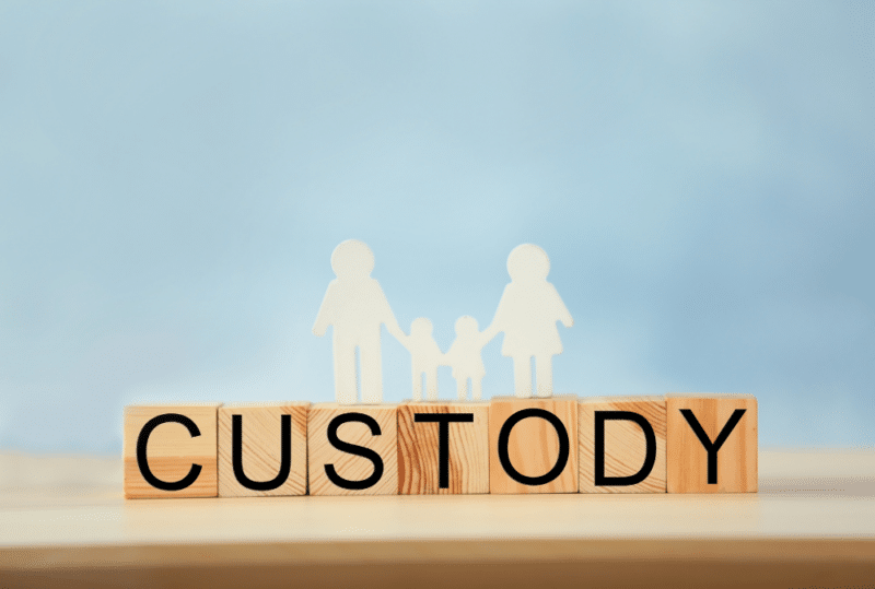 Image is of wooden alphabet blocks that spells the word 'custody' with paper figures of two adults and two children against a blue backdrop, concept of the requirements for child custody in Tennessee