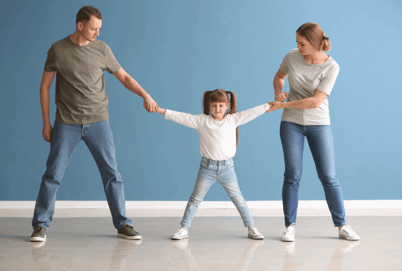 Image is of a young girl standing between her parents while they are pulling her in different directions, concept of child choosing which parent to live with in Tennessee