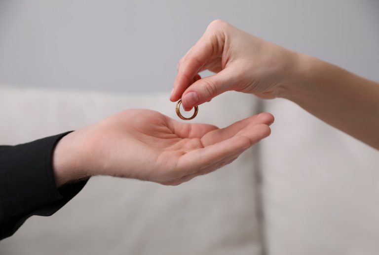 Image is of a woman dropping her wedding band into the open hand of man's hand, concept of how forgiving adultery can affect divorce case