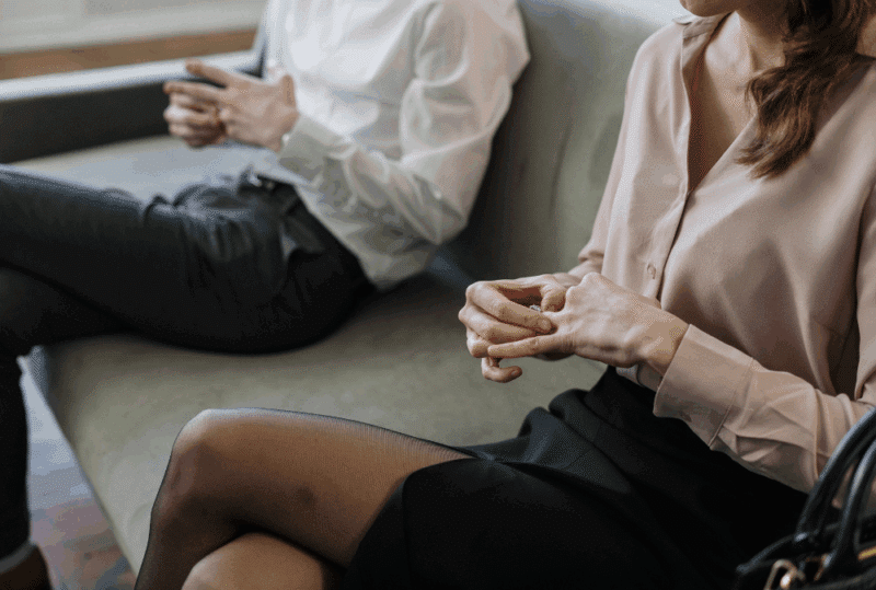 Image is of a man and woman sitting on a couch, both are twisting their wedding rings, concept of waiting periods for a divorce in Tennessee