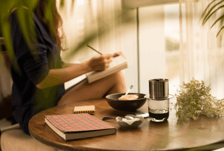 Image is of a relaxed woman writing in a journal sitting next to a table with tea and flowers, concept of tips for a less stressful divorce in Franklin