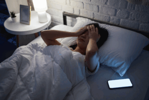 Image is of a woman upset in her bed at night with her phone on next to her, concept of how social media can ruin your divorce case