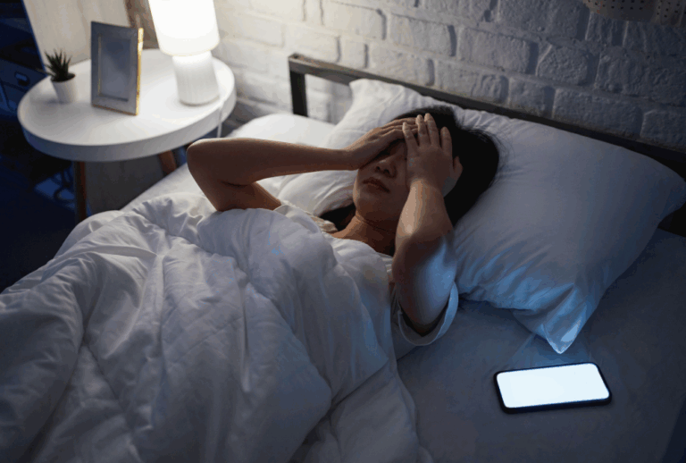 Image is of a woman upset in her bed at night with her phone on next to her, concept of how social media can ruin your divorce case
