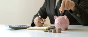 Person adding coins to piggy bank while writing notes about dividing retirement accounts in a Tennessee divorce.