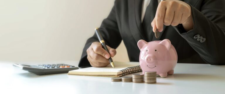Person adding coins to piggy bank while writing notes about dividing retirement accounts in a Tennessee divorce.