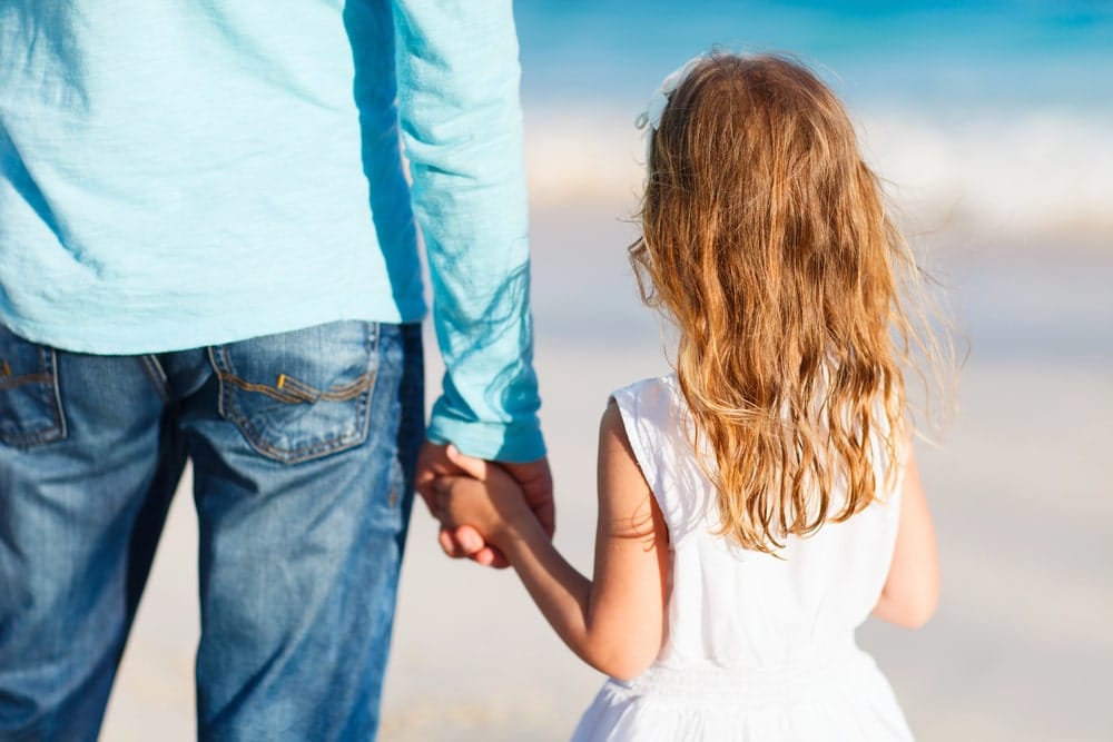 Father holding daughter’s hand at beach showing family bonding under shared custody schedules