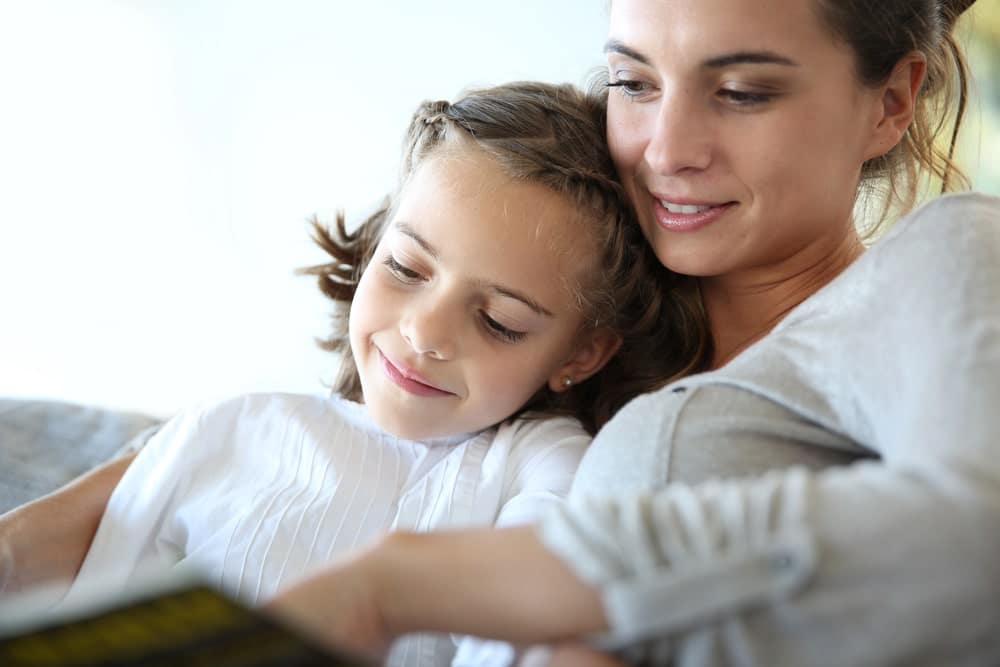 Image is of a mother reading with her young daughter on a couch, concept of nurturing care in situations involving child custody and unmarried parents.