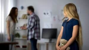 Image shows a young girl holding a teddy bear while her parents argue in the background, concept of parental alienation in Tennessee.