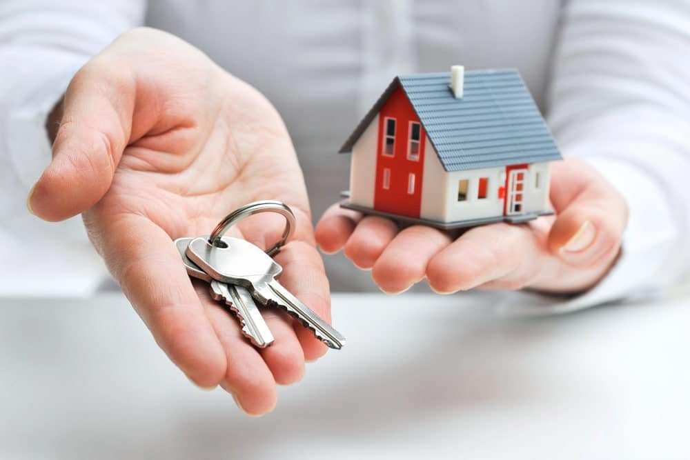 Image shows a person holding a house model and keys, concept of property division and home ownership decisions in a Franklin divorce.