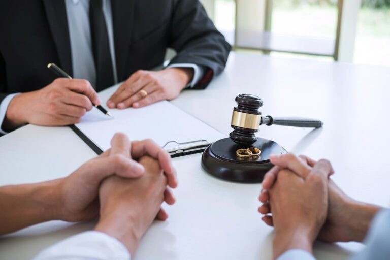 Image is of a couple sitting across from a lawyer who is writing on a clipboard, showing a legal consultation during the divorce process.