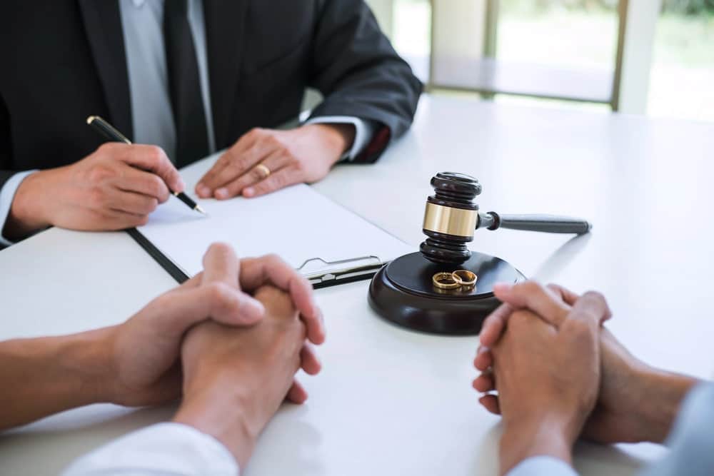 Image is of a couple sitting across from a lawyer who is writing on a clipboard, showing a legal consultation during the divorce process.