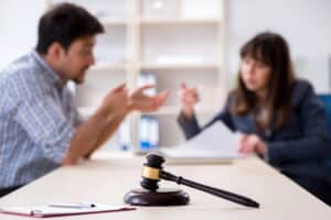 Image is of a court gavel in focus with a legal discussion happening in the background, representing how divorce affects taxes during legal proceedings