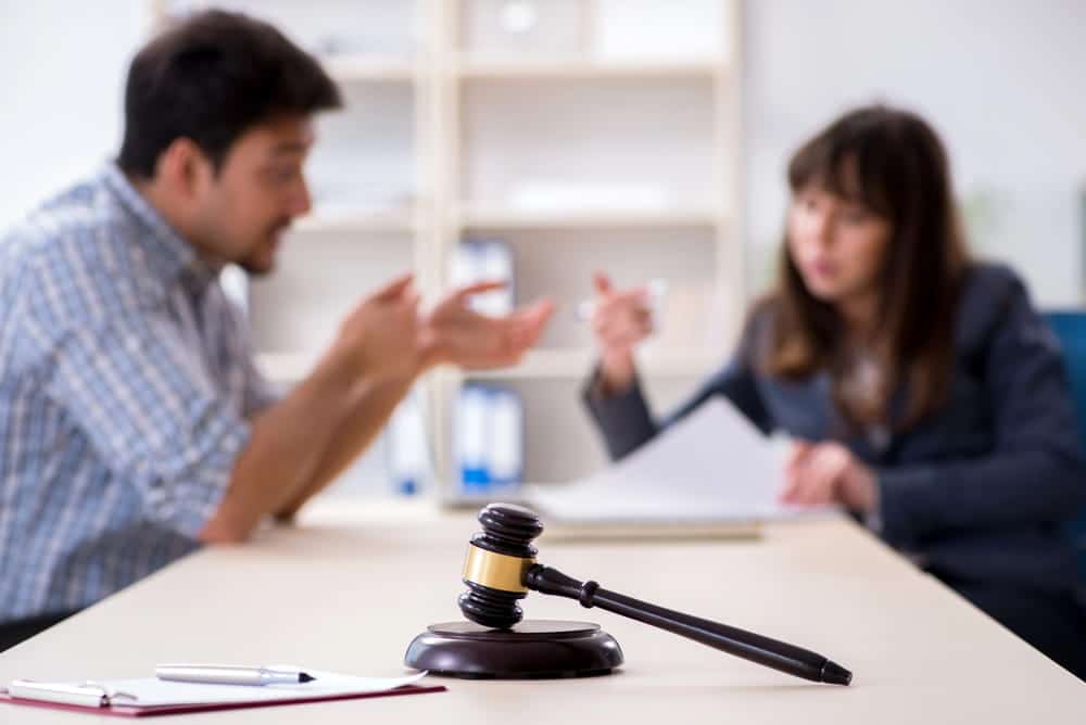 Image is of a court gavel in focus with a legal discussion happening in the background, representing how divorce affects taxes during legal proceedings