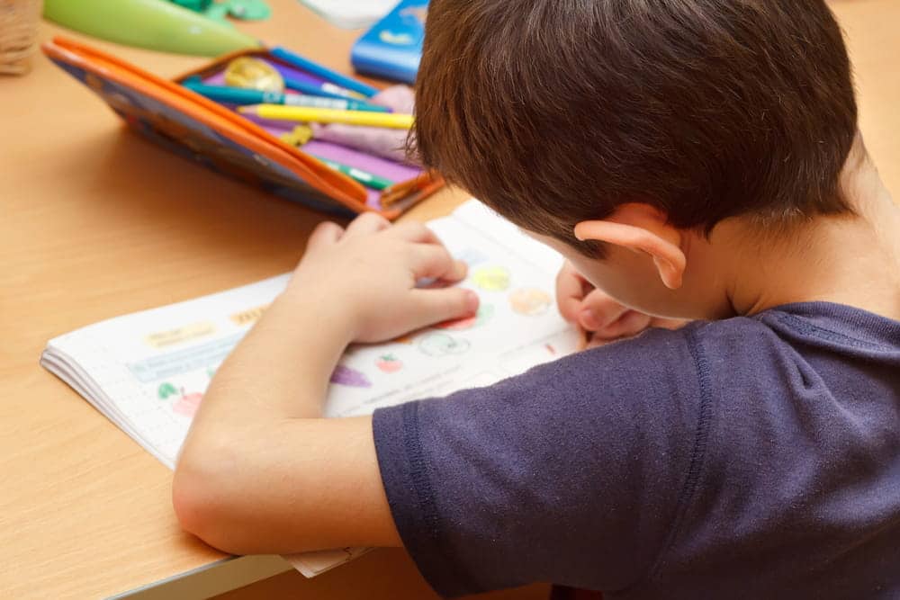 Image is of a young child doing homework at a desk, highlighting daily routines and stability considerations in child custody matters.