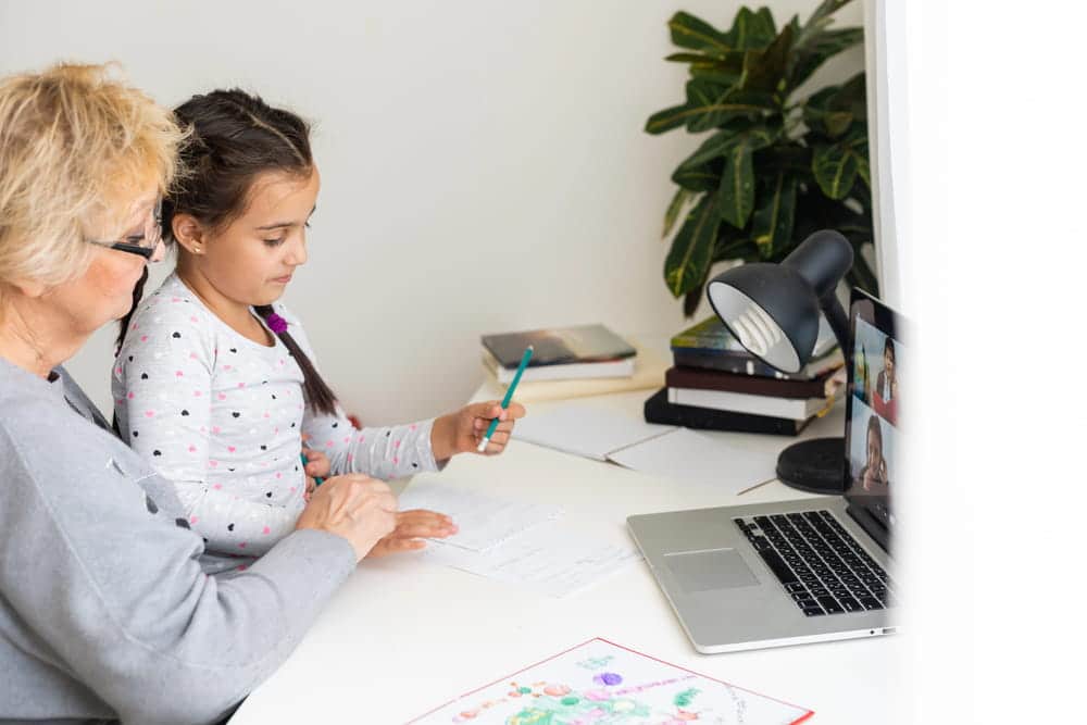 Image is of a grandparent assisting a child with schoolwork during a video call, reflecting caregiving roles in child custody situations.