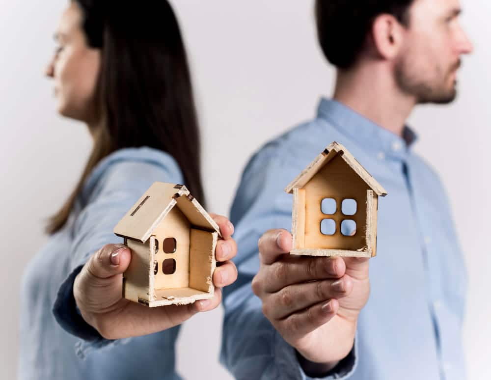 Image is of a separated couple holding small wooden houses while standing back to back, symbolizing property disputes in divorce in Franklin.