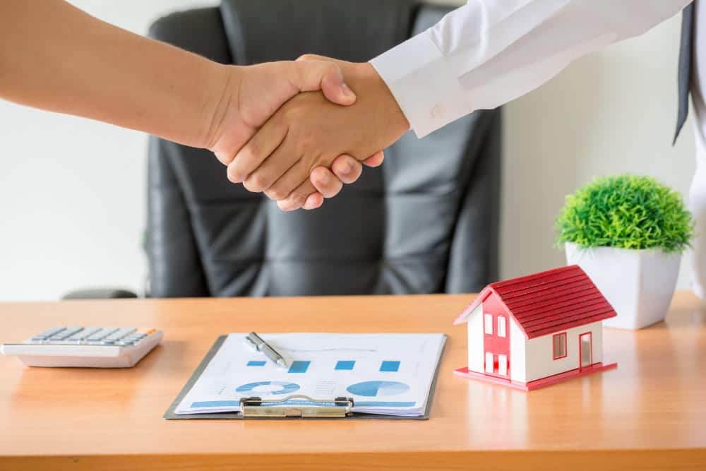 Image is of two individuals shaking hands over paperwork with a model home on the desk, representing negotiation during divorce in Franklin.