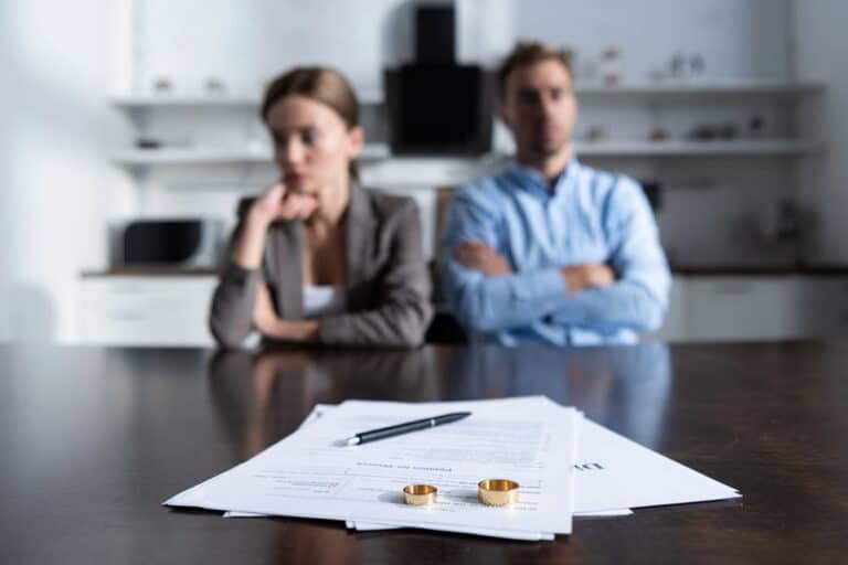 Image is of a separated couple sitting apart with divorce papers and wedding rings on the table, concept of divorce in Franklin legal separation.