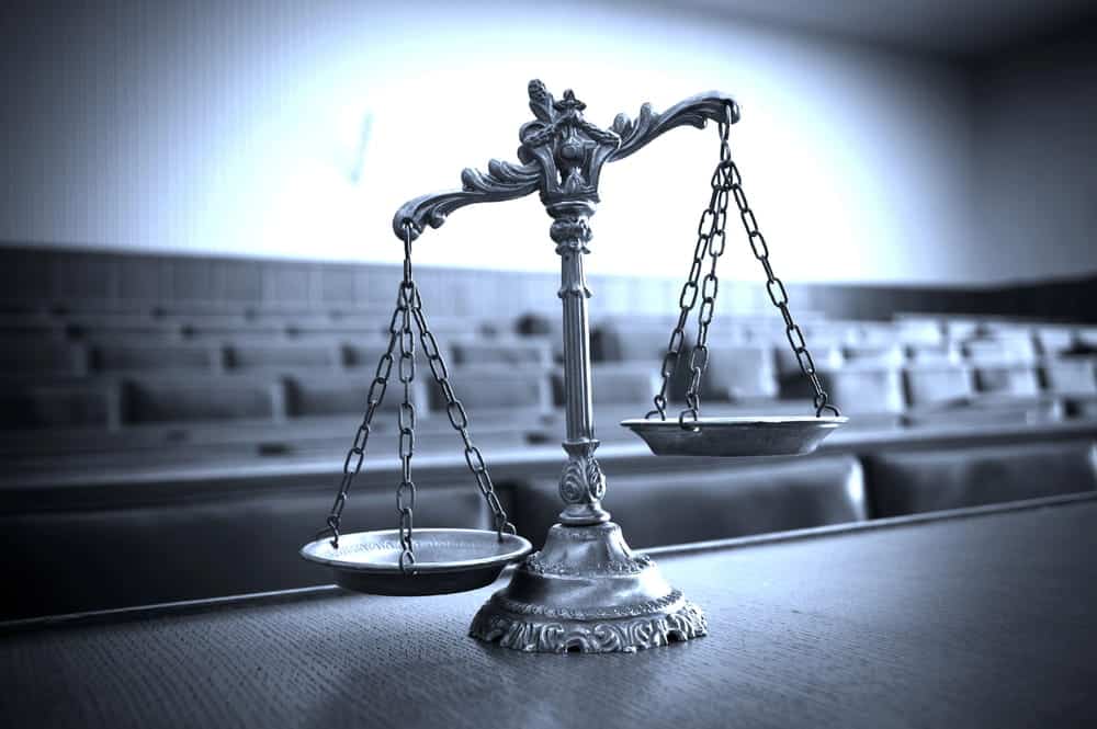Image is of a silver scale of justice sitting on a wooden table in an empty courtroom, concept of divorce mediation