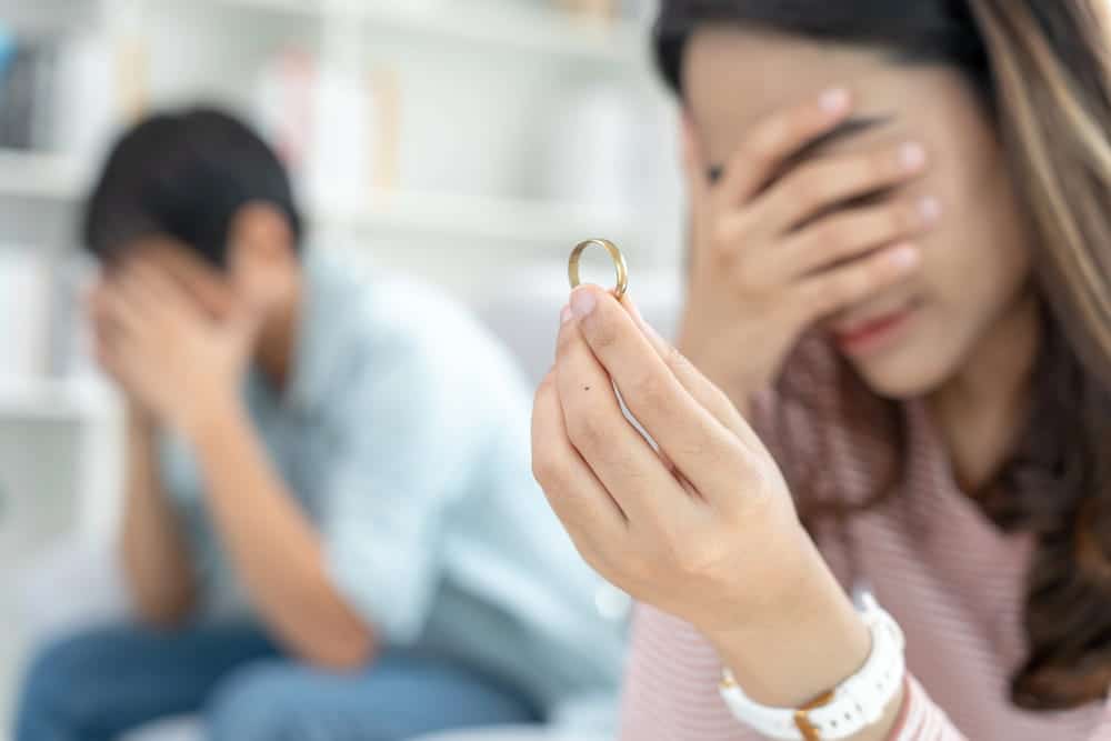 Image is of a woman holding a wedding ring while both partners appear distressed, concept of divorce in Franklin