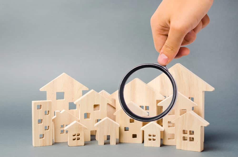 Image is of a hand holding a magnifying glass over multiple house models, symbolizing review of high net worth divorce assets