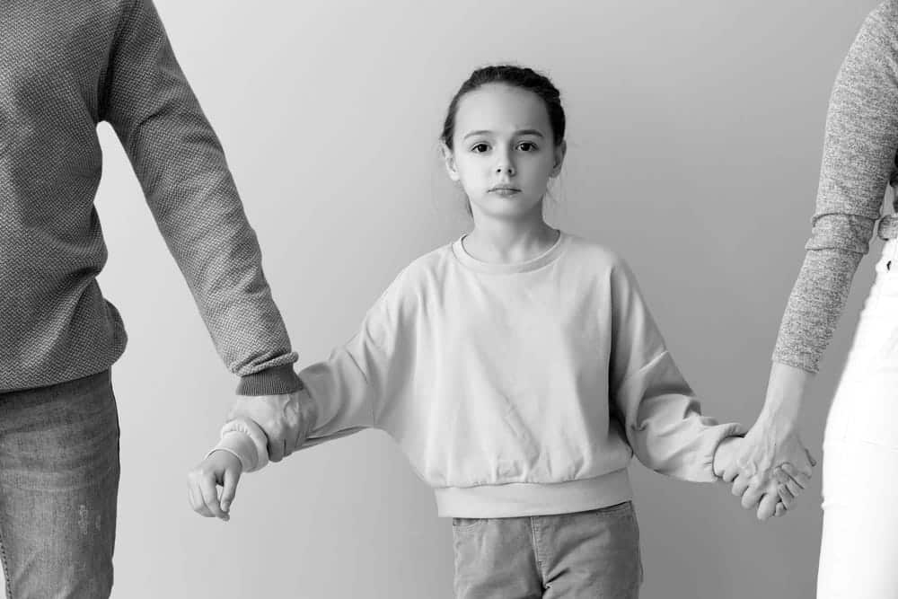 Image is of a child standing between separated parents holding each hand, concept of a Franklin contested divorce lawyer assisting with child custody and parenting disputes.