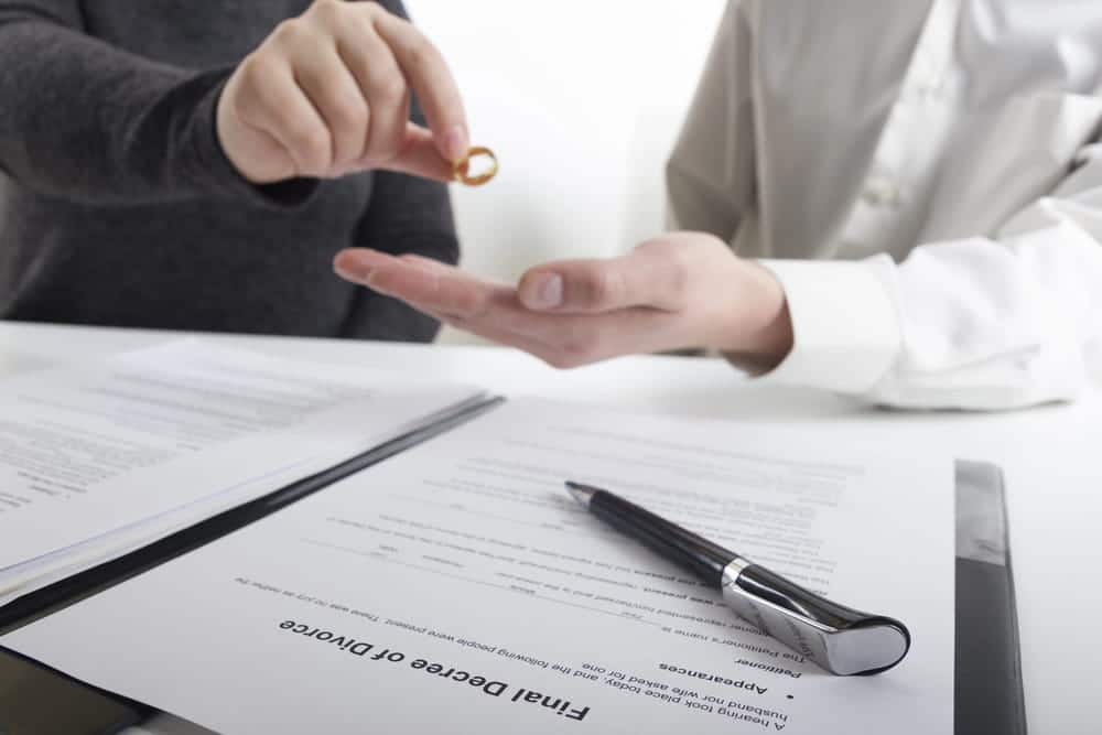Image is of spouses exchanging a wedding ring over divorce paperwork during a legal separation process, concept of Franklin uncontested divorce lawyer handling mutual divorce agreements.