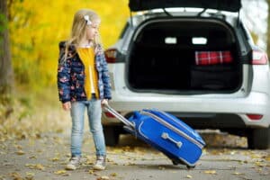Image is of a young child standing near a vehicle with luggage during a custody exchange, concept of holiday travel arrangements after divorce in Franklin.
