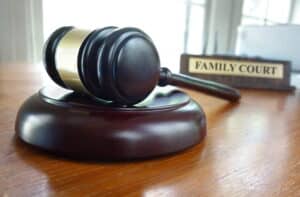 Image is of a courtroom gavel placed beside a family court sign, concept of legal consequences and enforcement proceedings involving a custody order violation.