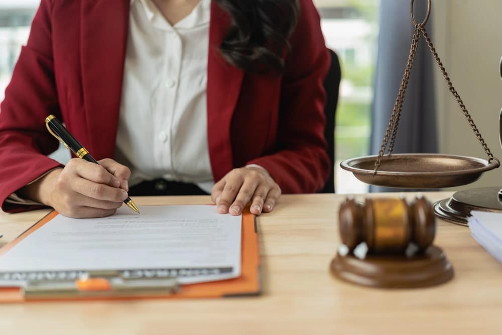 Image is of a person signing legal paperwork beside scales of justice, concept of a divorce without children lawyer.