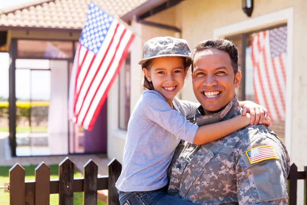 Image is of a service member holding a child outside a home, concept of military divorce lawyer helping families resolve child custody matters.