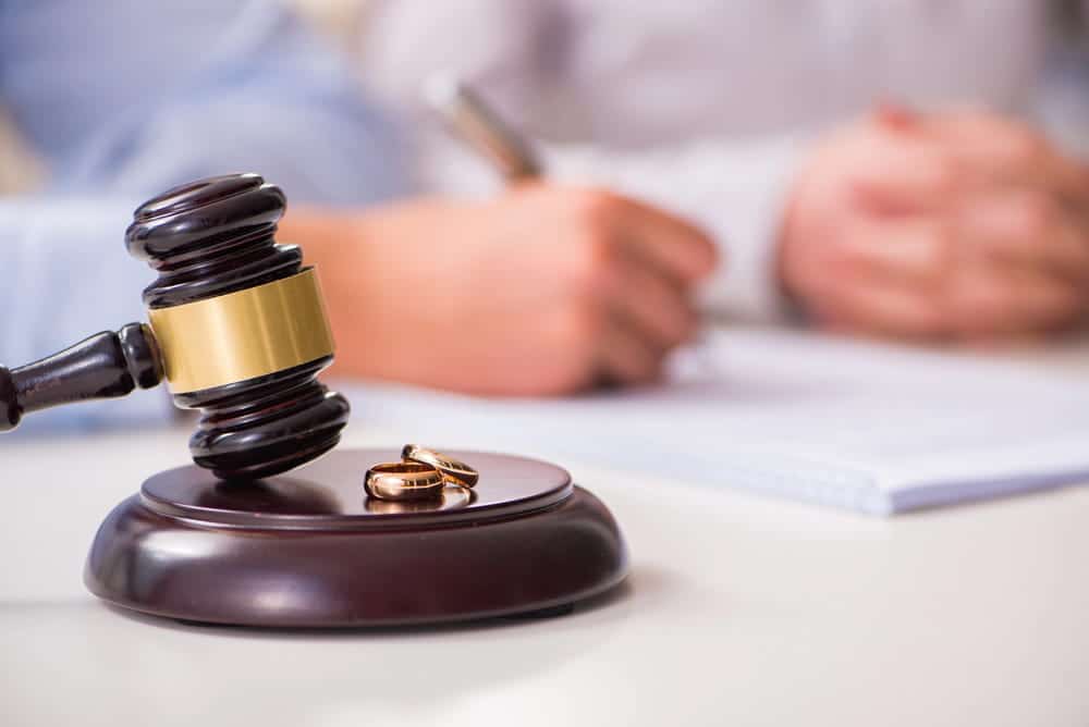 Image is of a judge's gavel beside wedding rings and legal documents, concept of military divorce lawyer representing clients during divorce proceedings.