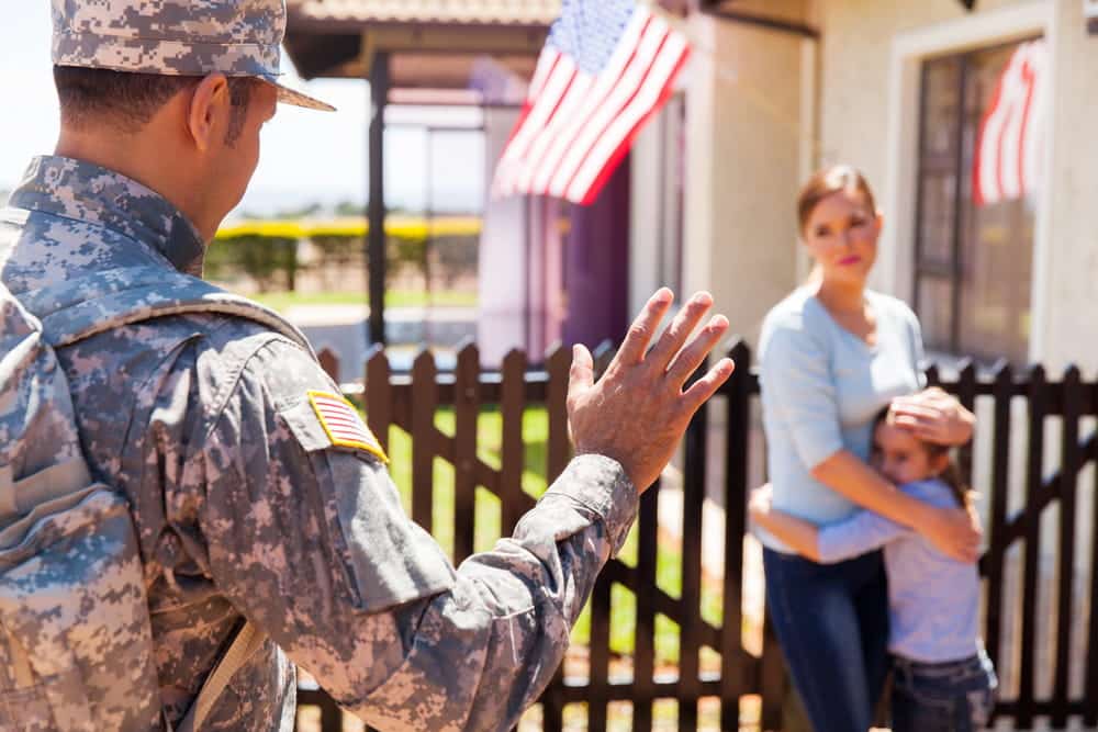 Image is of a service member speaking with family outside a home, concept of military divorce lawyer helping families address custody and deployment concerns.