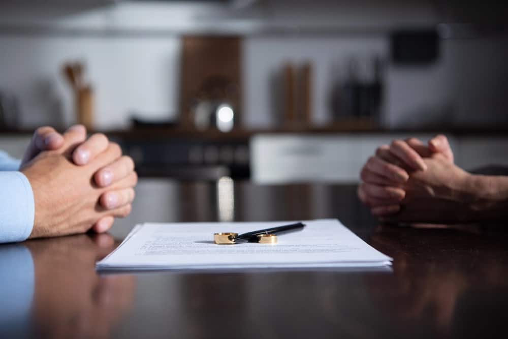 Image is of two people seated across from each other with divorce documents and wedding rings on the table, concept of a modifications of divorce decrees lawyer.