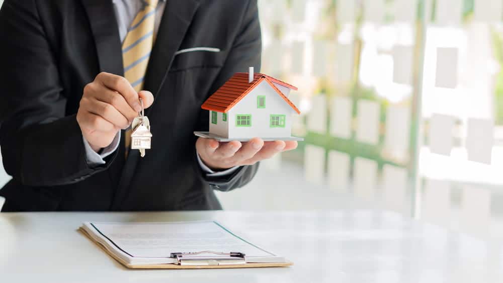 Image is of a professional holding a model home and house keys, concept of transferring property ownership as part of estate planning in Franklin following divorce.