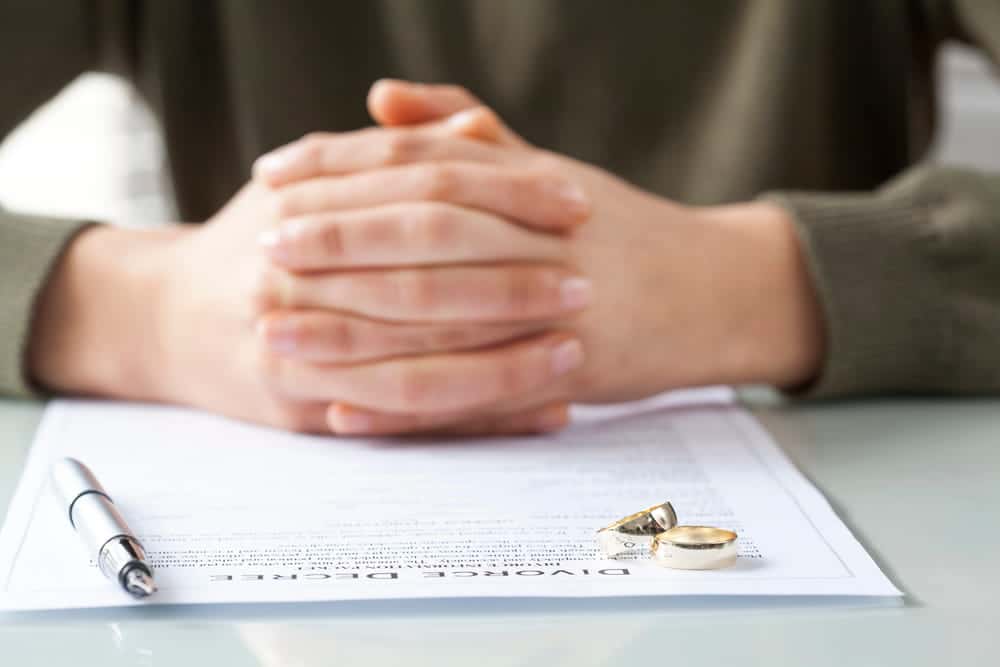 Image is of a person sitting with divorce papers and wedding rings, concept of requesting a name change during a Tennessee divorce.